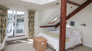 A bedroom with a sloped ceiling, a bed, a window with curtains, and a view of a hillside. - Fastnet at Nonsuch House (Dartmouth)