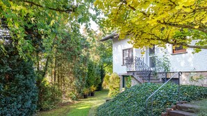 Une maison avec un escalier en pierre, un jardin avec un chemin dallé et une haie.