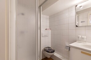 Ein Badezimmer mit weißen Fliesen, einer Toilette mit gemustertem Sitz, einem Waschbecken und einem Spiegel.