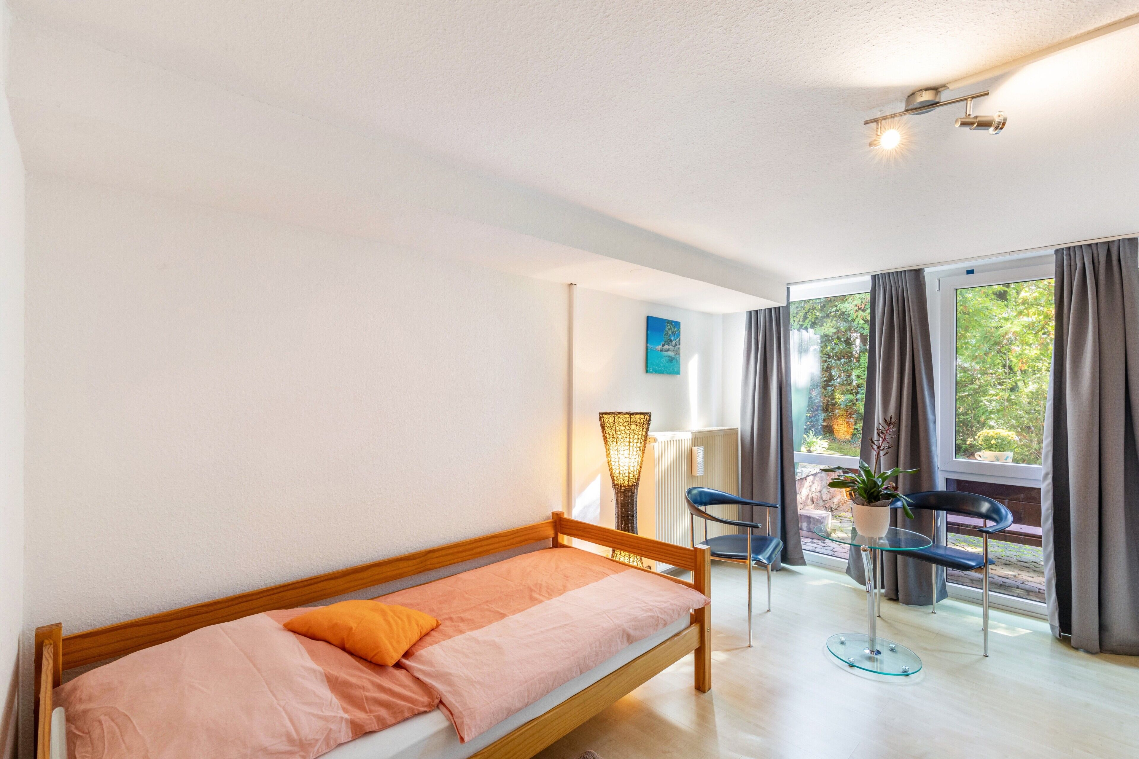 Una habitación con una cama individual, una silla, una mesa con una planta y vistas amplias por las ventanas.