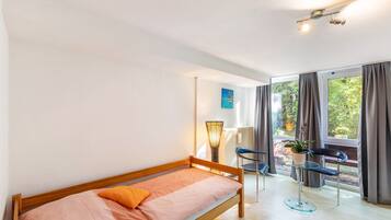 Una habitación con una cama individual, una silla, una mesa con una planta y vistas amplias por las ventanas.