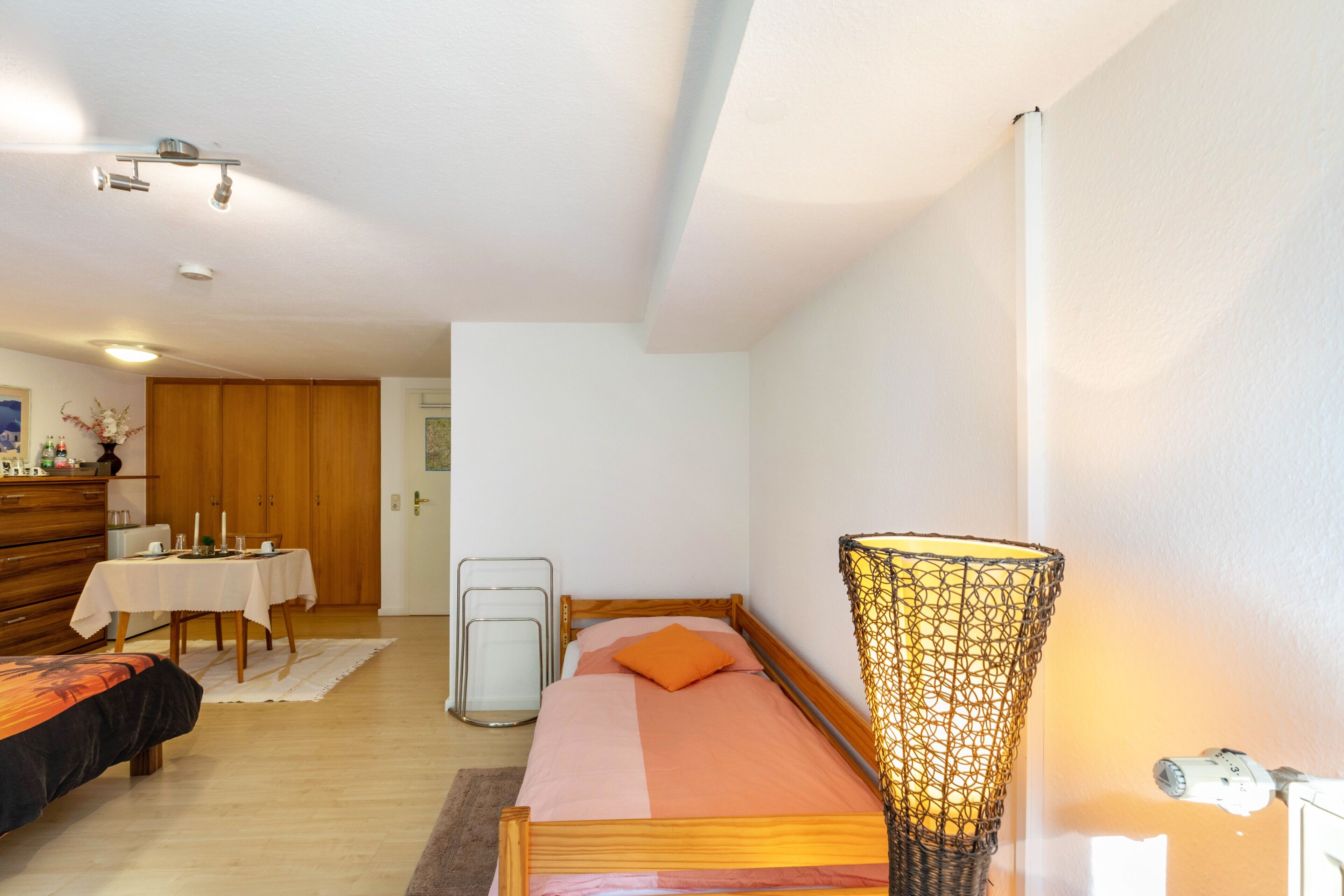 Une chambre à coucher comprenant un lit, une table de chevet, une lampe et donnant sur la salle à manger.