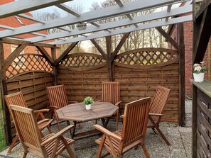 A wooden outdoor patio with a round table and six chairs, surrounded by a wooden fence with lattice designs. - Huus an't Zingel - Holiday home in Krummhörn-Rysum (Krummhörn)