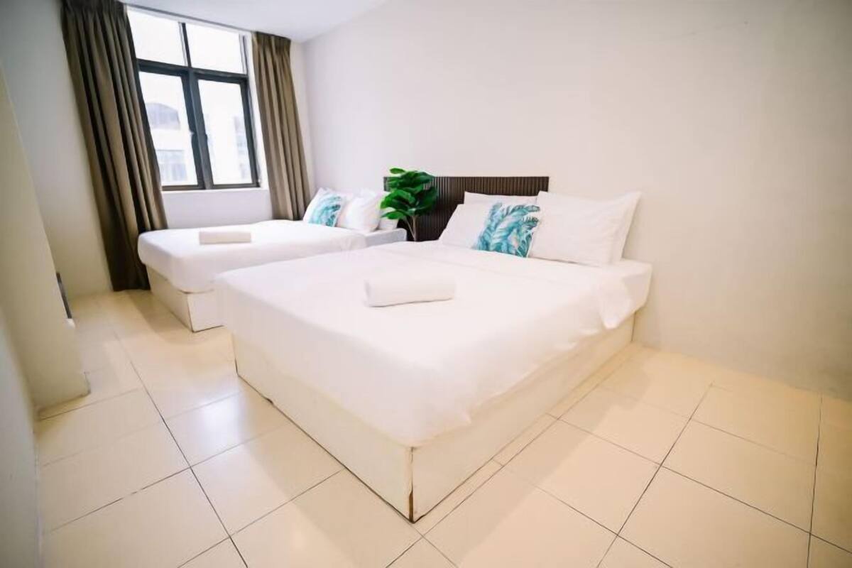 Een hotelkamer met twee bedden, een raam met gordijnen, een plant en een betegelde vloer.