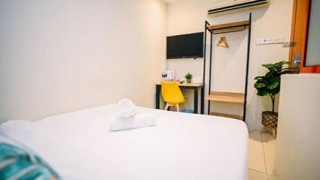Habitación de hotel con cama, escritorio, silla, televisor y planta en maceta.