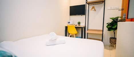 Habitación de hotel con cama, escritorio, silla, televisor y planta en maceta.