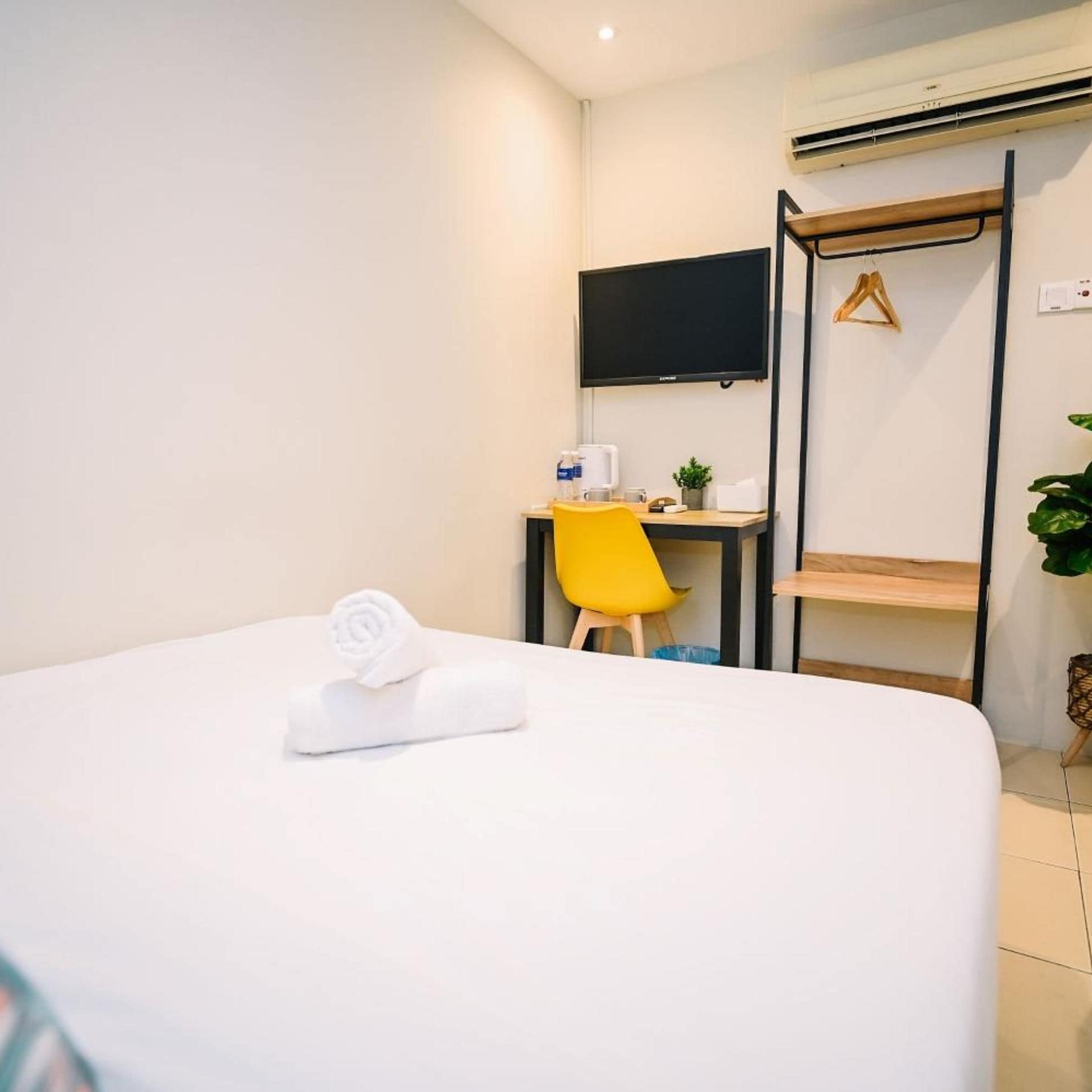 Ett hotellrum med en säng, ett skrivbord med en stol, en tv och en växt.