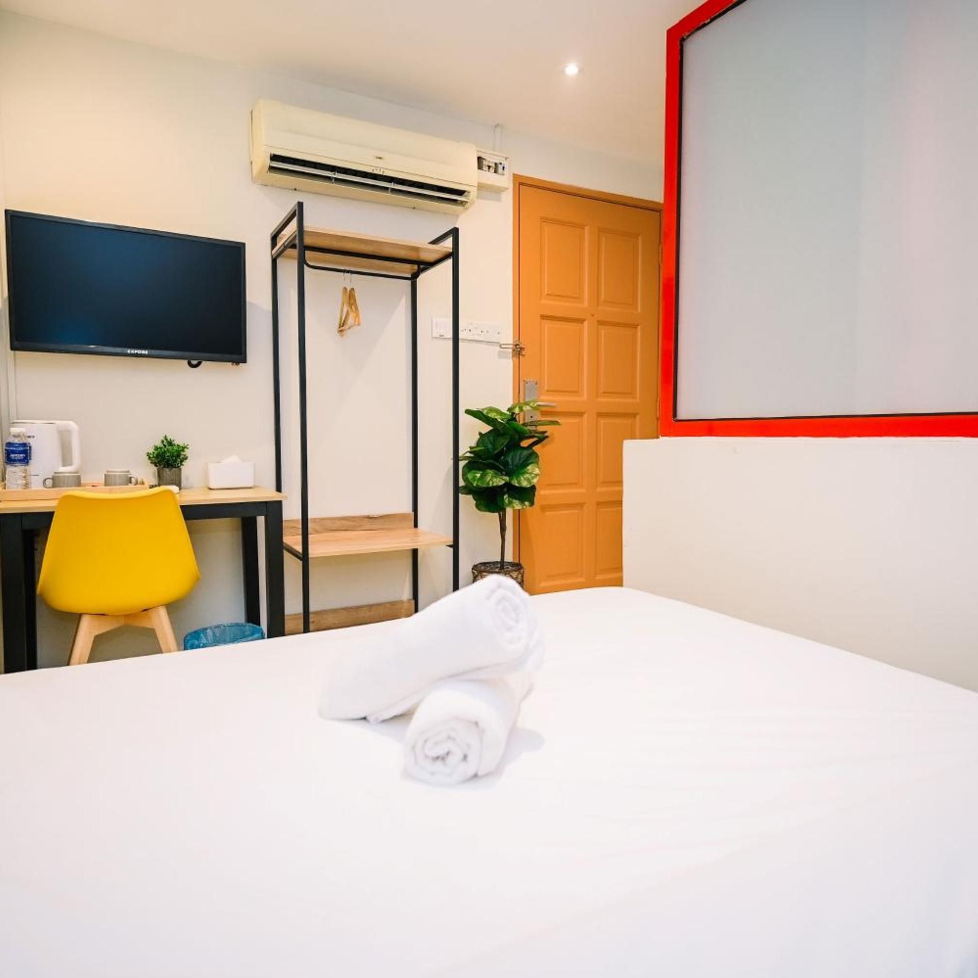 Una camera d'albergo con un letto, una scrivania con una sedia, un televisore e un condizionatore d'aria.