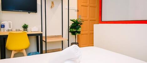 A hotel room with a bed, a desk with a chair, a television, and an air conditioning unit.
