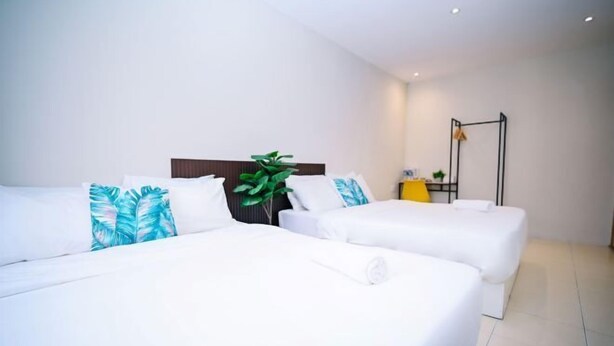 Une chambre d’hôtel avec deux lits, une plante, un bureau et un luminaire suspendu.