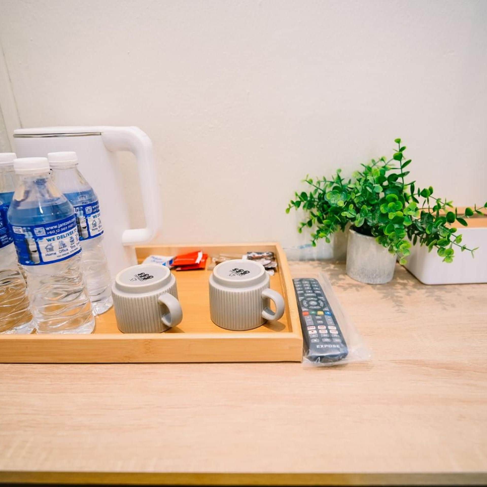 Una bandeja con dos tazas blancas, un control remoto y agua embotellada sobre una superficie de madera.