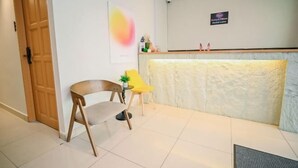Un espace d’accueil avec une porte en bois, un comptoir de réception, une chaise jaune et une petite table sur laquelle est posée une plante.