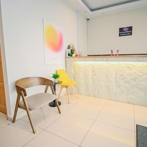 Un espace d’accueil comprenant une chaise en bois, une chaise jaune, un comptoir d’accueil et un panneau fixé au mur.