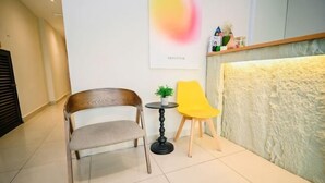 Un espace d’accueil comprenant une chaise en bois, une chaise jaune, une petite table avec une plante et une étagère murale sur laquelle sont disposés divers objets.