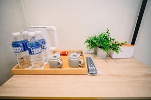 Un plateau en bois contenant des bouteilles d’eau, deux tasses, une télécommande et une plante en pot, le tout posé sur une table.
