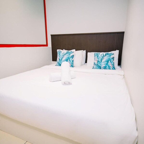 A neatly made bed with white linens and two pillows with a leaf pattern, a dark headboard, and a red accent on the wall.