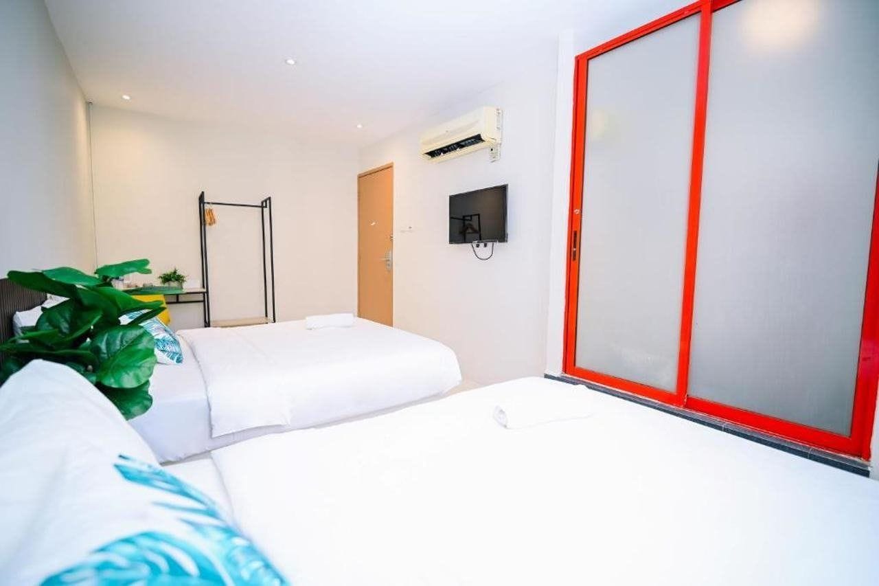 Habitación de hotel con cama, puerta corredera de marco rojo, televisor montado en la pared y equipo de aire acondicionado.