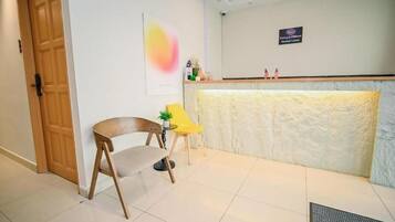 A reception area with a wooden door, a reception desk, a yellow chair, and a small table with a plant.
