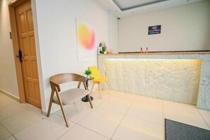 A reception area with a wooden door, a reception desk, a yellow chair, and a small table with a plant. - Swing & Pillows @ KL Kuchai Lama (Kuala Lumpur)