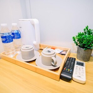 Un plateau contenant deux bouteilles d’eau, deux tasses blanches, une télécommande, un téléphone et une plante en pot.