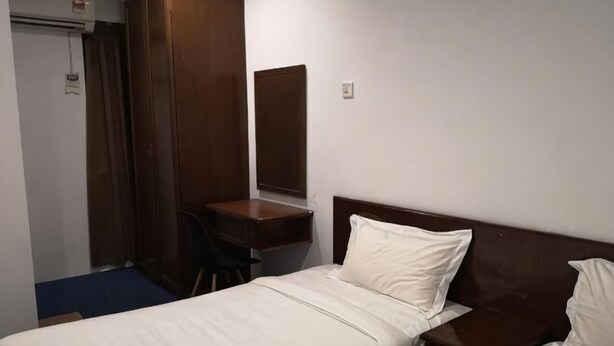 Habitació d'hotel amb un llit individual, un panell de capçalera de fusta, un escriptori petit i un mirall.