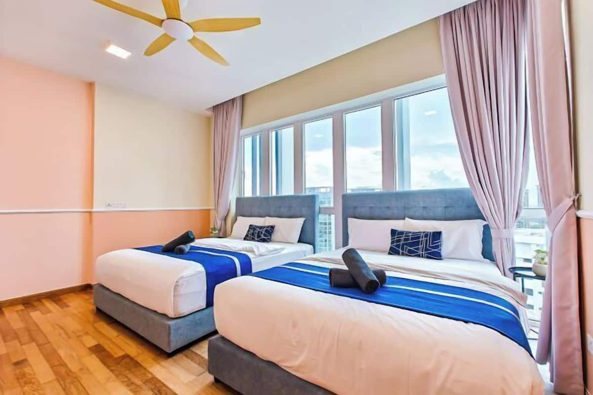 Habitación de hotel con dos camas, ventilador de techo, ventanas amplias y vista a la ciudad.