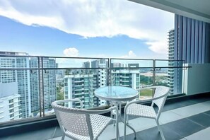 Un balcon avec une table en verre et deux fauteuils en osier, donnant sur un paysage urbain avec de hauts immeubles.