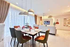 Un espace de repas moderne avec une table dressée pour quatre personnes, un canapé et un téléviseur en arrière-plan.
