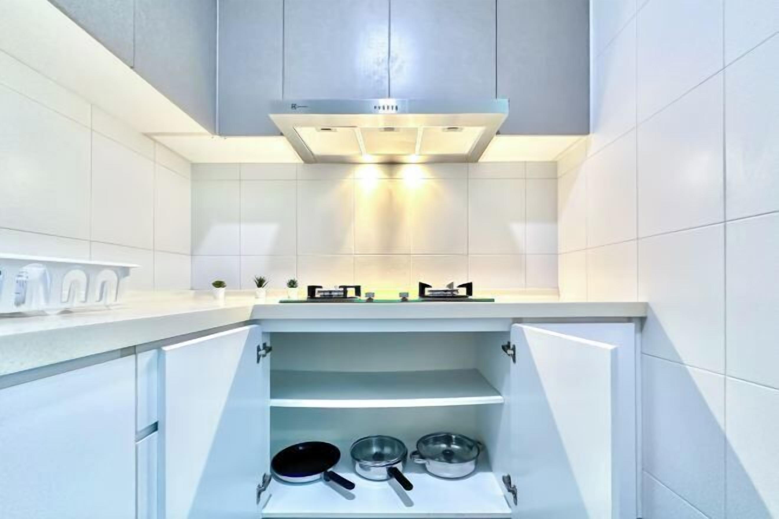 Una cuina moderna amb armaris blancs, una campana extractora d'acer inoxidable i una prestatgeria integrada amb recipients de cuina.