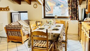 A cozy dining area with a wooden table set for two, a sofa, and a window with a view of a building.