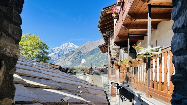 A mountain view from a building with a wooden balcony, stone roof, and a clear sky.