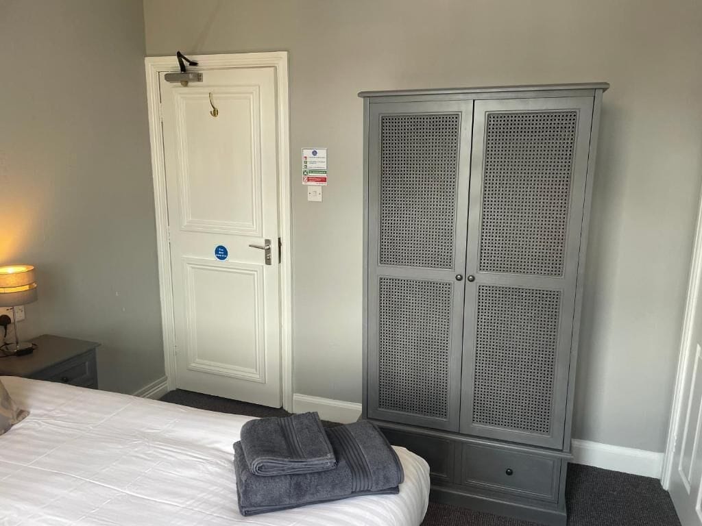 A hotel room with a bed, a white door, and a grey wardrobe.