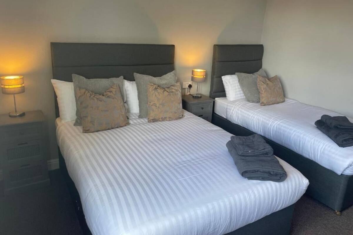 A hotel room with two beds, each with a headboard, bedside tables, lamps, and pillows.