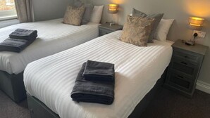 A hotel room with two beds, each with a pillow and a folded towel. There are bedside lamps on each nightstand. - The Nags Head (York)