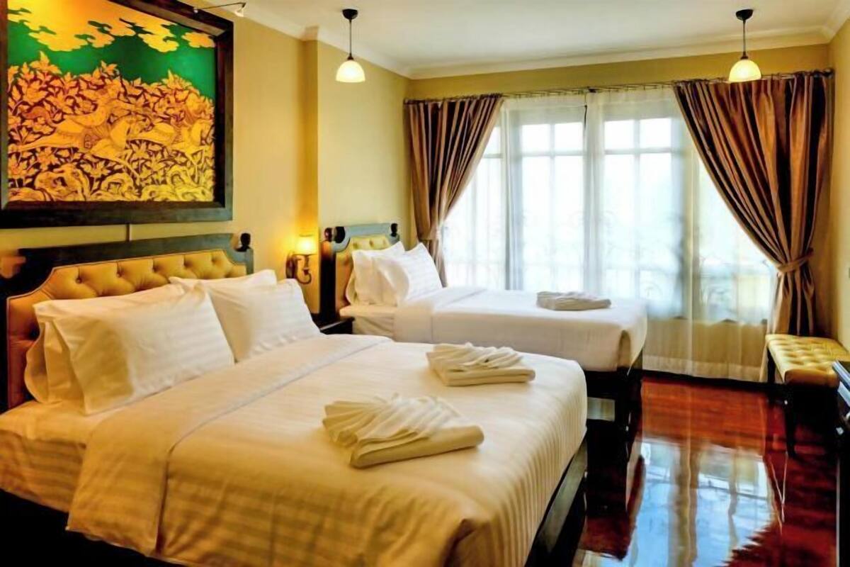 A hotel room with two beds, a large painting on the wall, and a window with curtains.