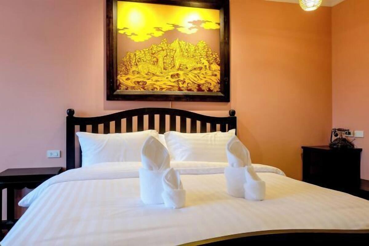 A neatly made bed with white linens and towels folded at the foot, a wooden headboard, and a framed artwork above the bed.