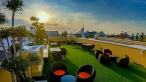 A rooftop terrace with artificial grass, wicker furniture, and a city skyline view. - Siri Heritage Bangkok Hotel (Bangkok)