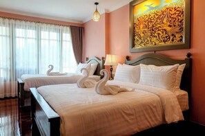 A hotel room with two beds, each with white linens and swan-shaped pillows. There is a painting on the wall above the beds and a lamp on the nightstand. - Siri Heritage Bangkok Hotel (Bangkok)