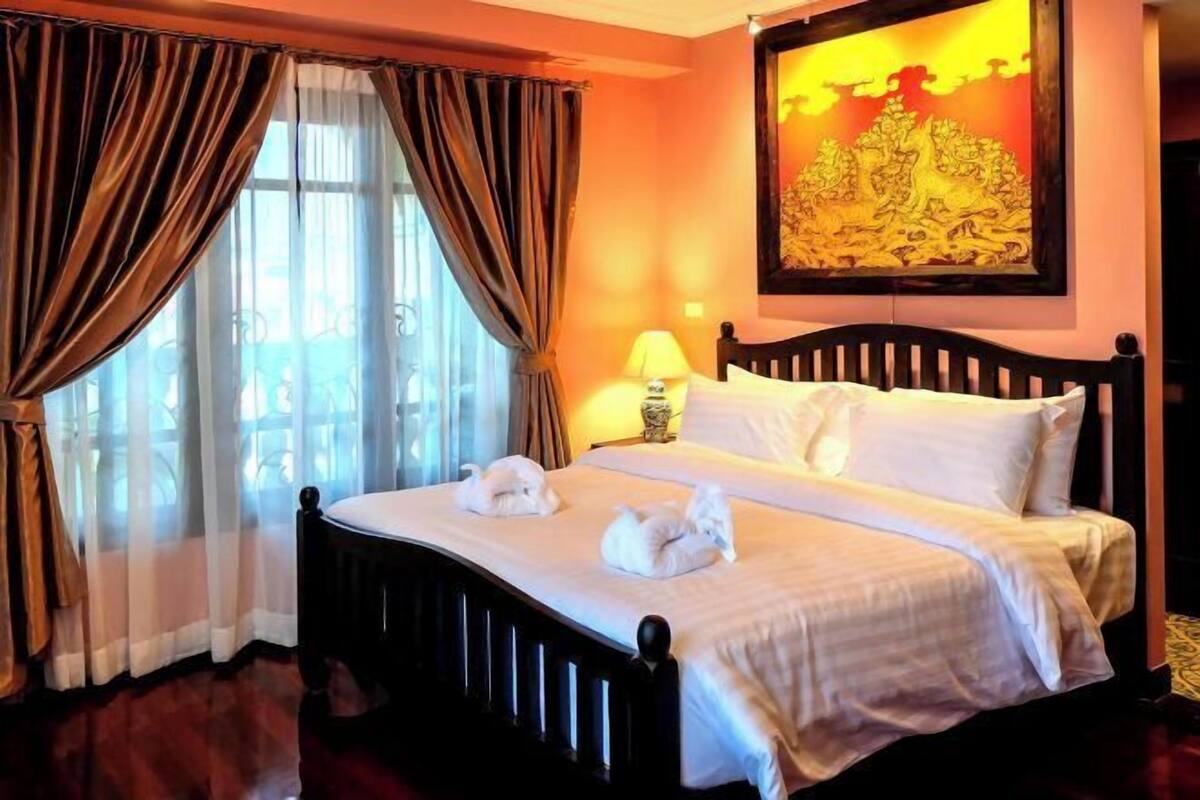 A hotel room with a bed, curtains, a lamp, and a painting on the wall.