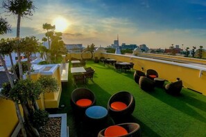 Una terraza en la azotea con mobiliario exterior, vistas del horizonte urbano y un atardecer.
