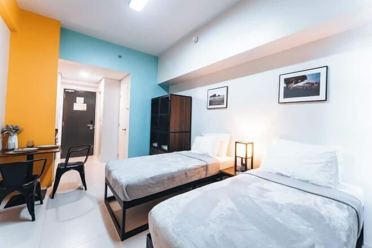 Una habitación con dos camas, un escritorio, sillas, un armario y cuadros en la pared.
