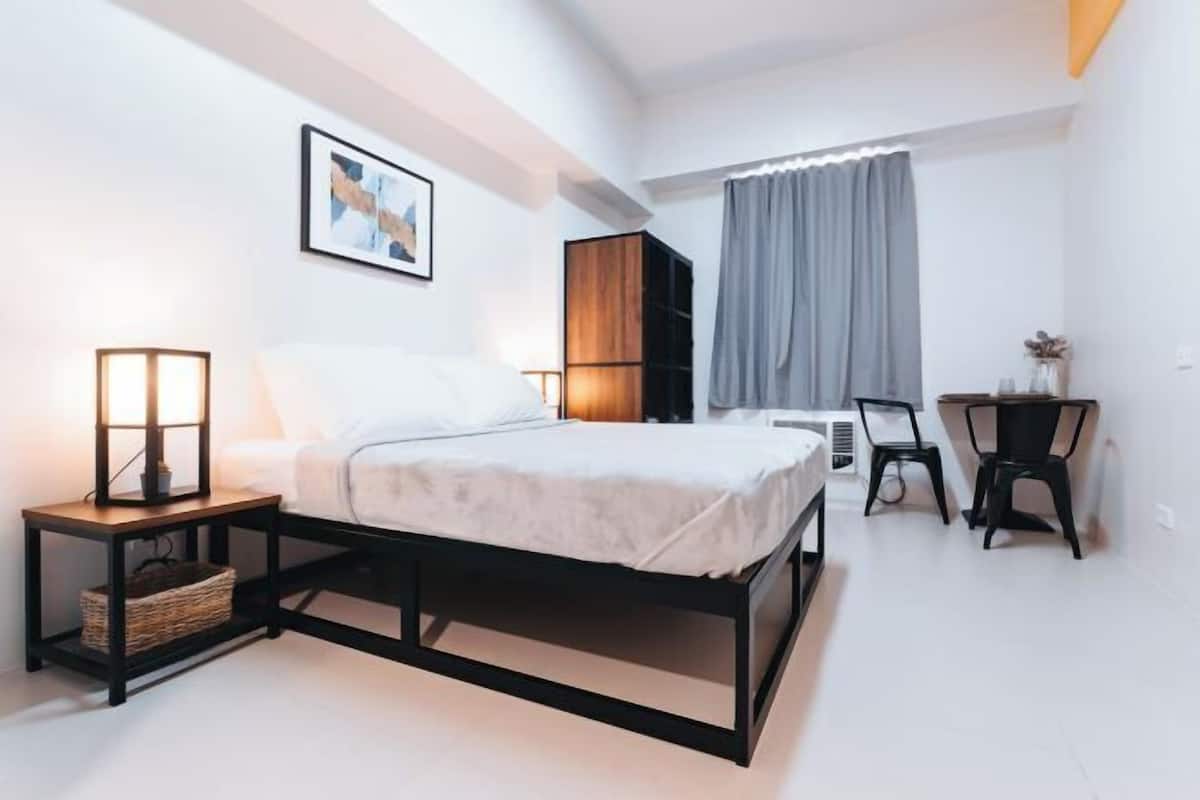 Un dormitorio moderno con cama, mesita de noche, lámpara y escritorio con silla.