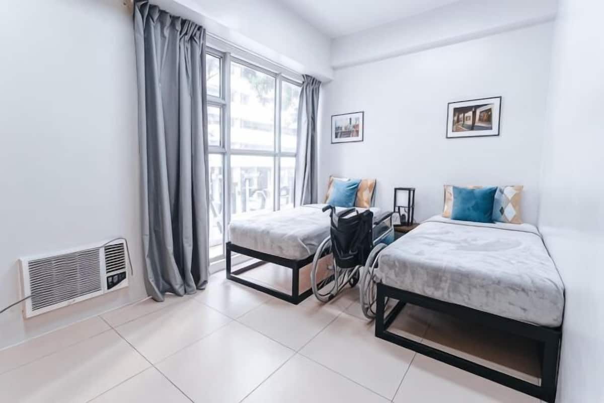 Un dormitorio con dos camas, una ventana con cortinas, un radiador y un cuadro colgado en la pared.