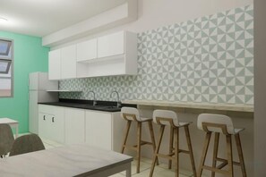 A kitchen with white cabinets, a black countertop, and a geometric backsplash. There are three white bar stools and a table. - The City Flats Circuit Makati (Makati)