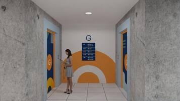 Corredor com uma pessoa em pé, uma placa com a letra 'G' e um painel de parede com um desenho circular.