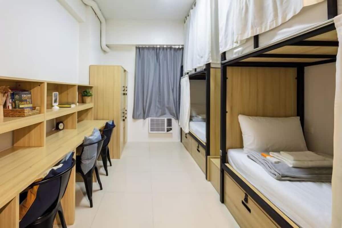 Una habitación tipo dormitorio compacta con literas, un escritorio, sillas y una kitchenette pequeña.