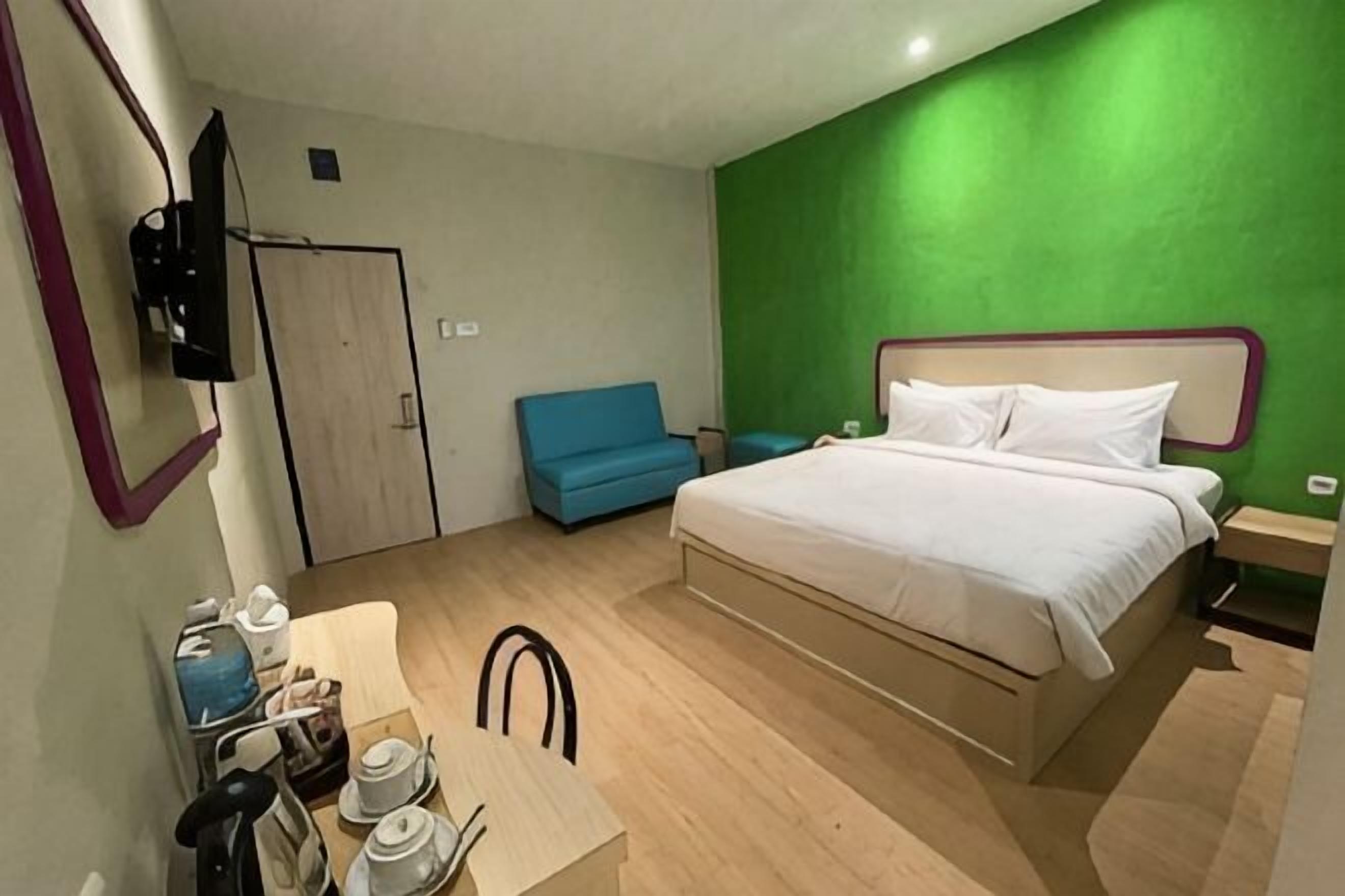 A bedroom with a bed, a desk with a chair, a blue sofa, and a green accent wall.