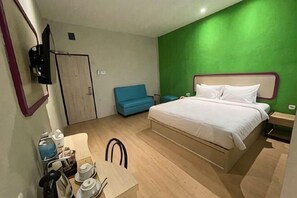 Ein Schlafzimmer mit einem Bett, einem Schreibtisch mit Stuhl, einem blauen Sofa und einer grünen Akzentwand.