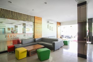 A modern cafe interior with a sofa, wooden coffee table, and colorful ottomans. - Rumaruma Hotel Kenten Palembang (Palembang)