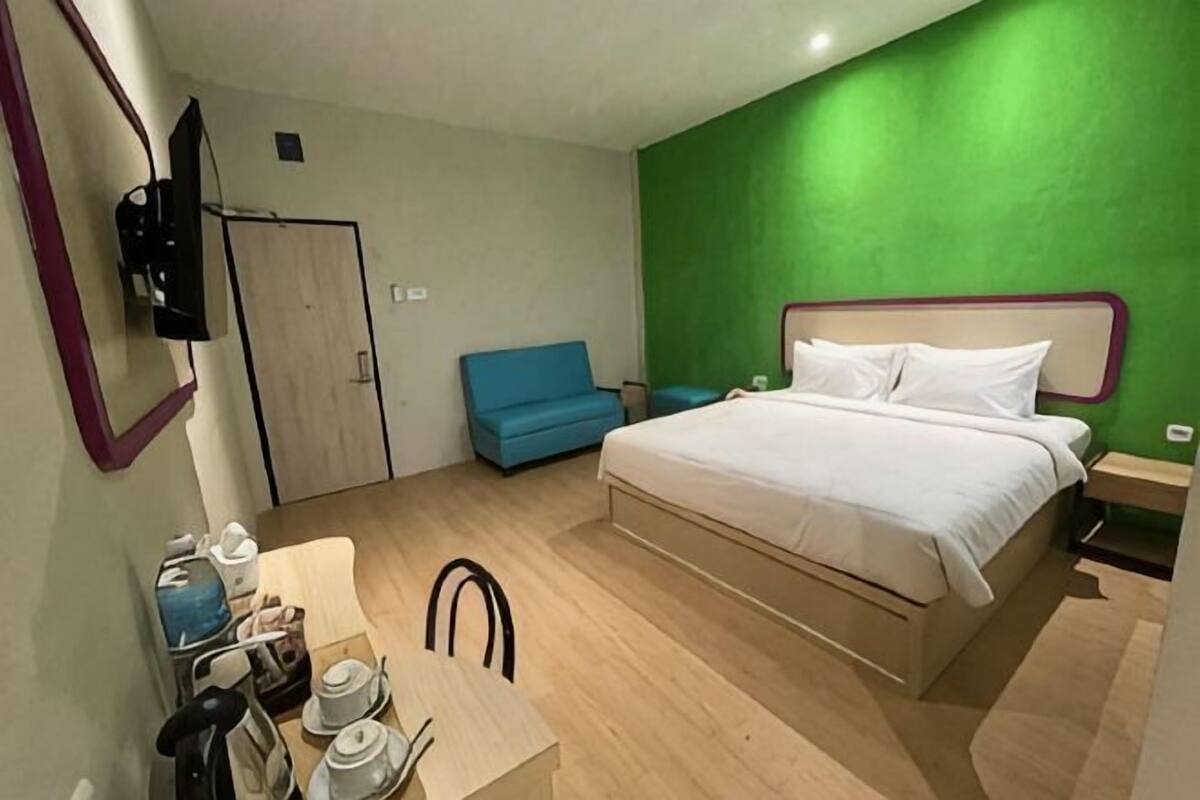 Une chambre  à coucher avec un lit, un bureau et une chaise, un canapé bleu et un mur d’accent vert.